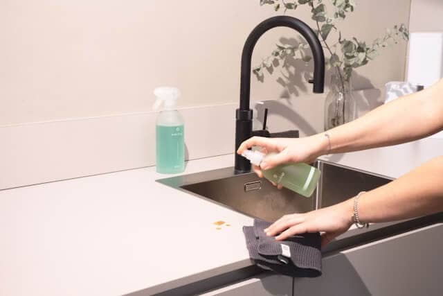 Someone mid-task — wiping a kitchen counter while on the phone or sipping coffee. Conveys “busy but doing it anyway.”