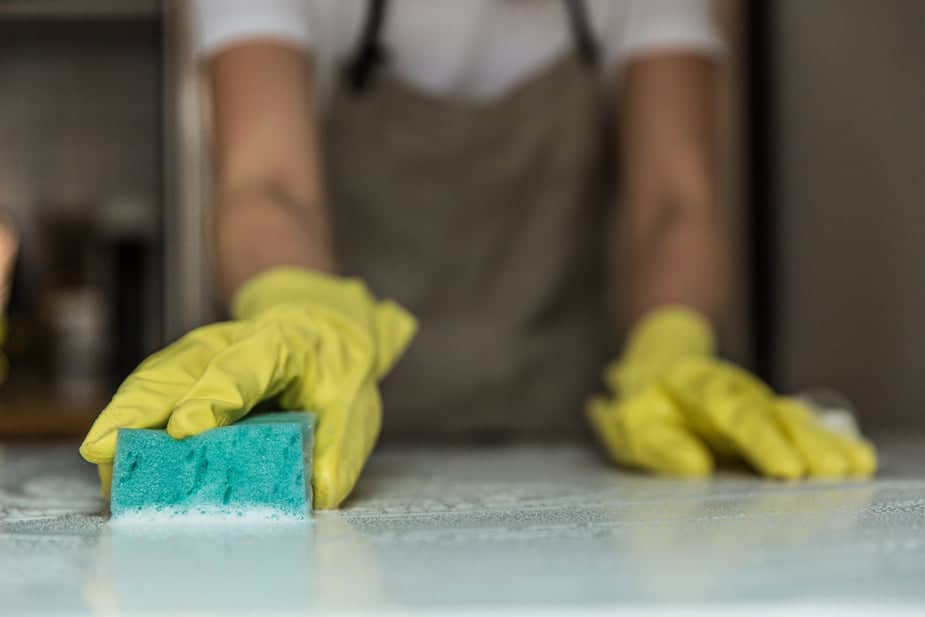 Person wearing yellow gloves scrubbing a sudsy countertop with a sponge